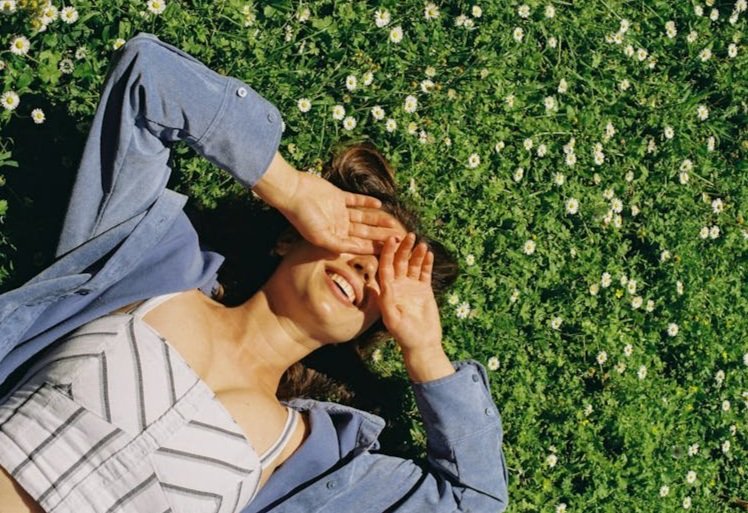 free-photo-of-smiling-woman-in-a-blue-blouse-and-white-striped-crop-top-lying-on-a-meadow